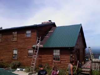 Green metal roof going on a two story log home with ladders set in Humboldt